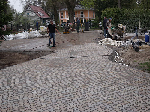 Der Sand in den Fugen wird befeuchtet, damit er sich setzt Pflasterung einer Einfahrt