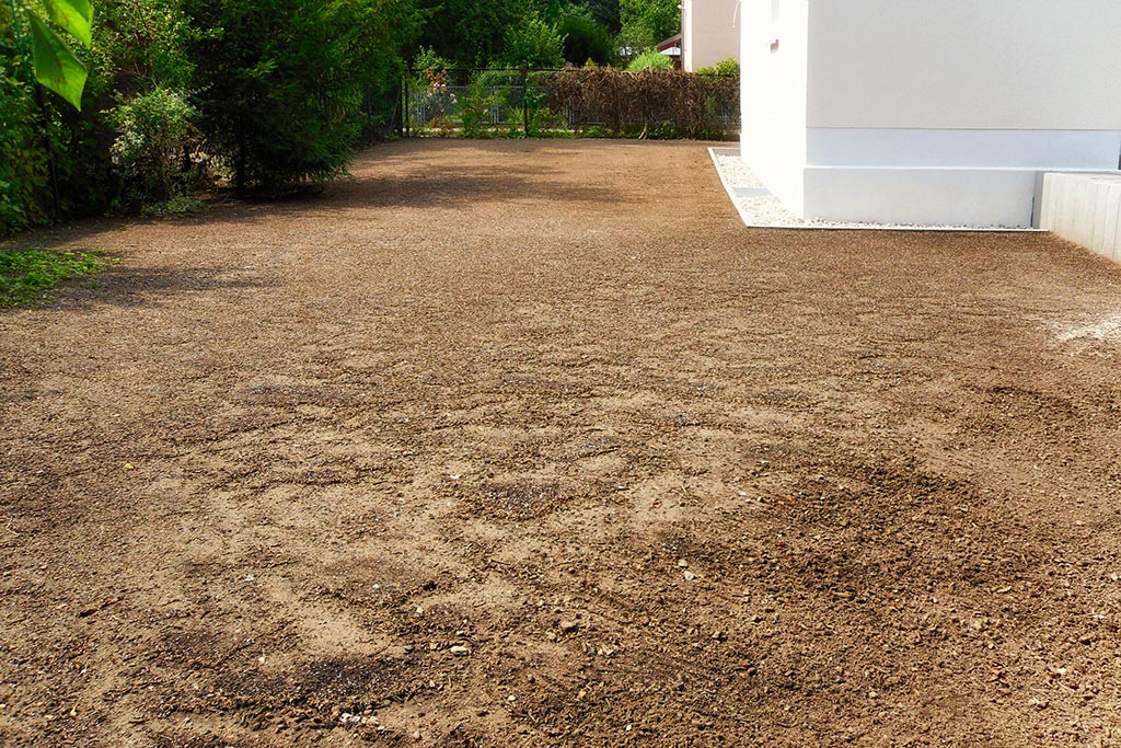 Gartenneuanlage nach Neubau - Traufkante am Haus mit weißen Kieseln und große Fläche mit Rasenaussaat
